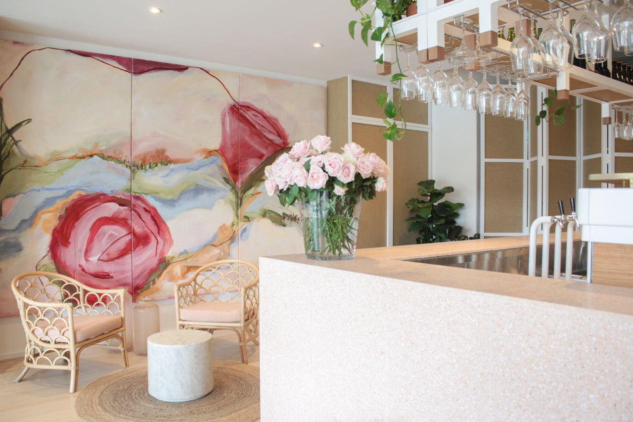 A mural painting of roses in soft tones behind a very sophisticated bar